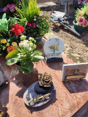 Différents ornements et plaques souvenirs sur une tombe en marbre rose.